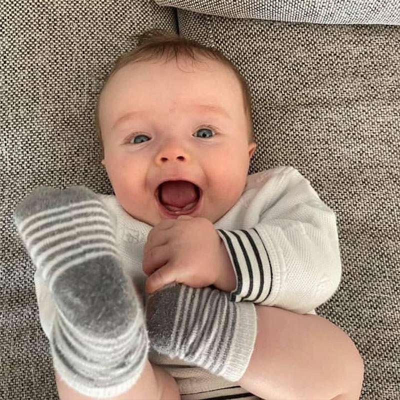 happy baby born via surrogacy in Canada with Canadian Fertility Consulting holding their feet with striped socks