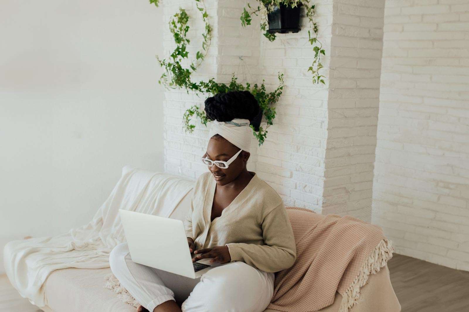 a black woman sitting on a cozy sofa with blankets, typing on her laptop researching about becoming a surrogate mother in canada