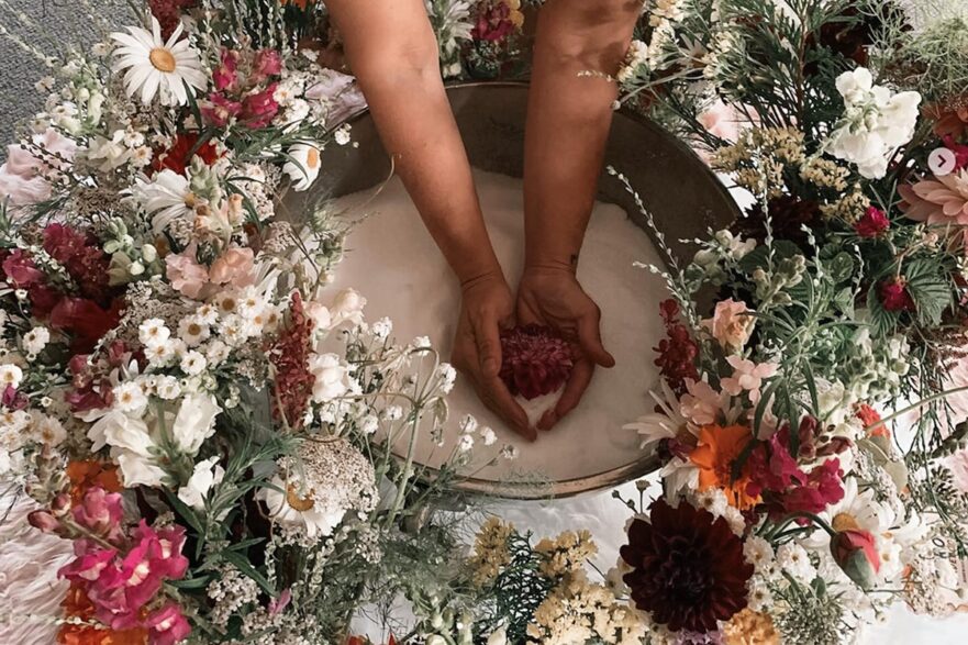 a surrogate places her hands in a salt bowl surrounded by beautiful flowers at a women's retreat in Nanaimo BC in July 2024