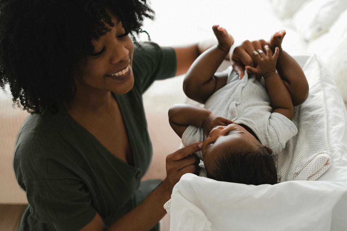 surrogate mother cradles her pregnant belly while her daughter leans in to kiss her mother’s growing baby bump. They are surrounded by luscious tropical plants and greenery.